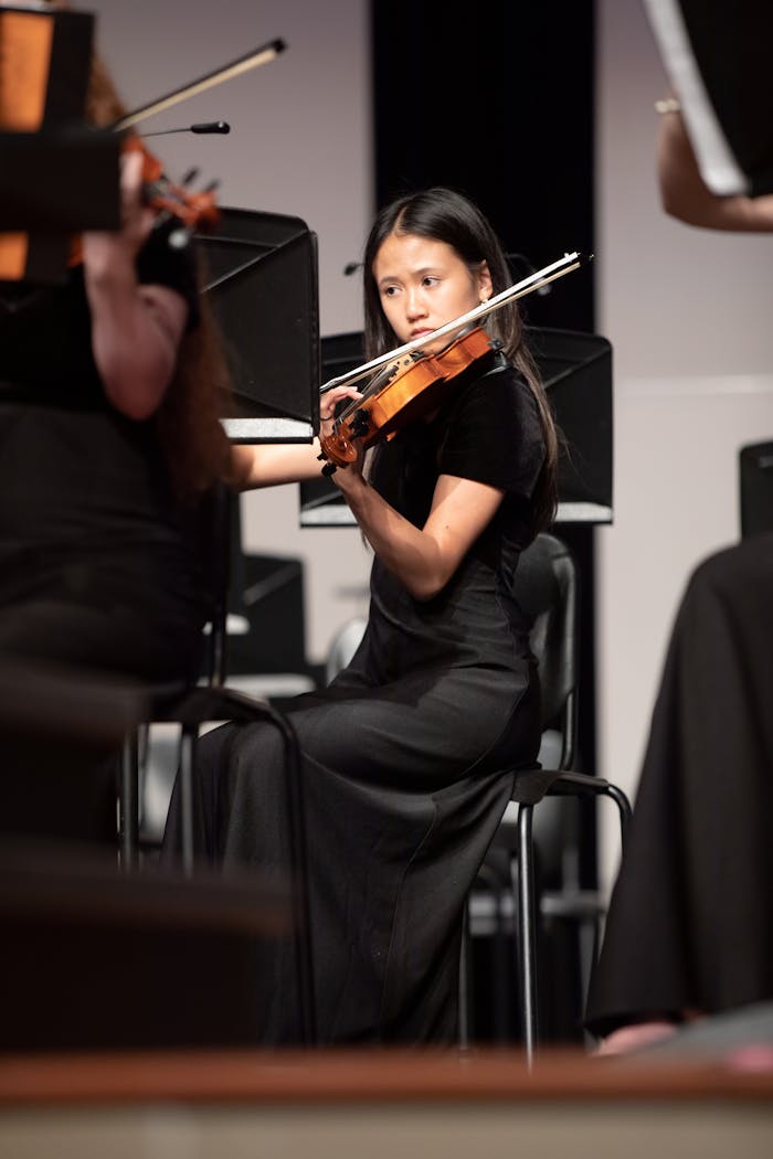 A young violinist in focus playing during an indoor orchestra performance.