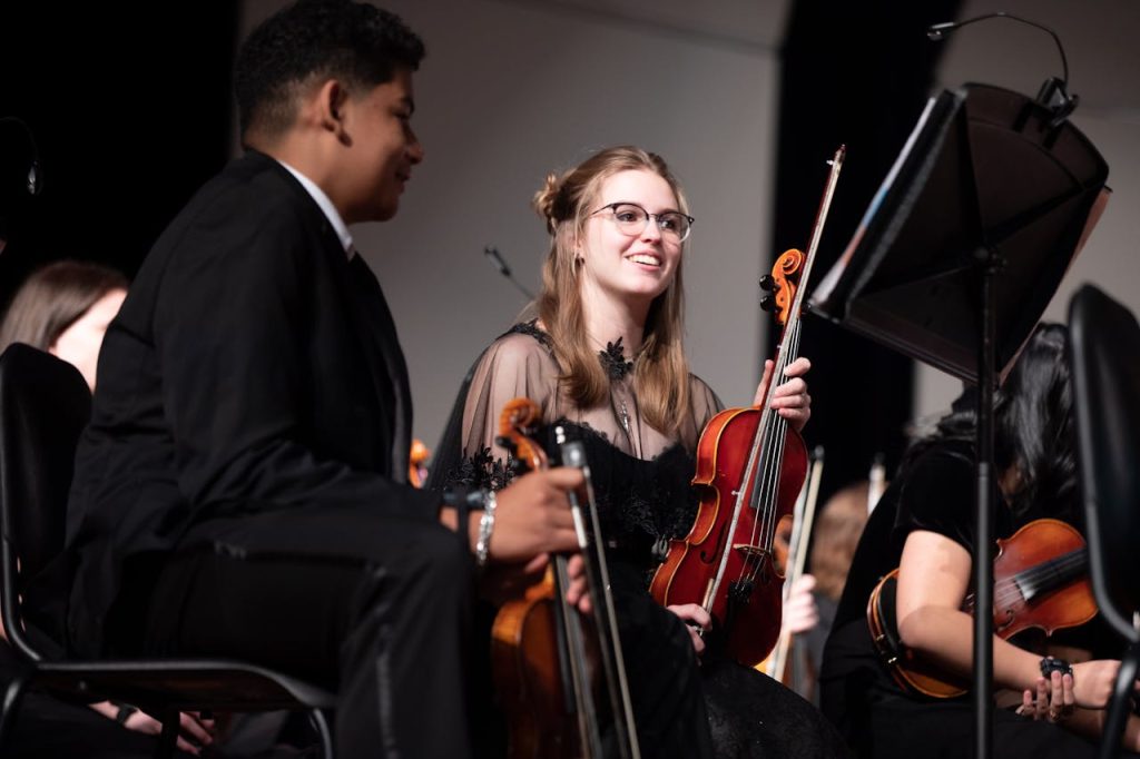 zipwp-image-12318287 Young musicians in formal attire performing with violins in an orchestra setting.